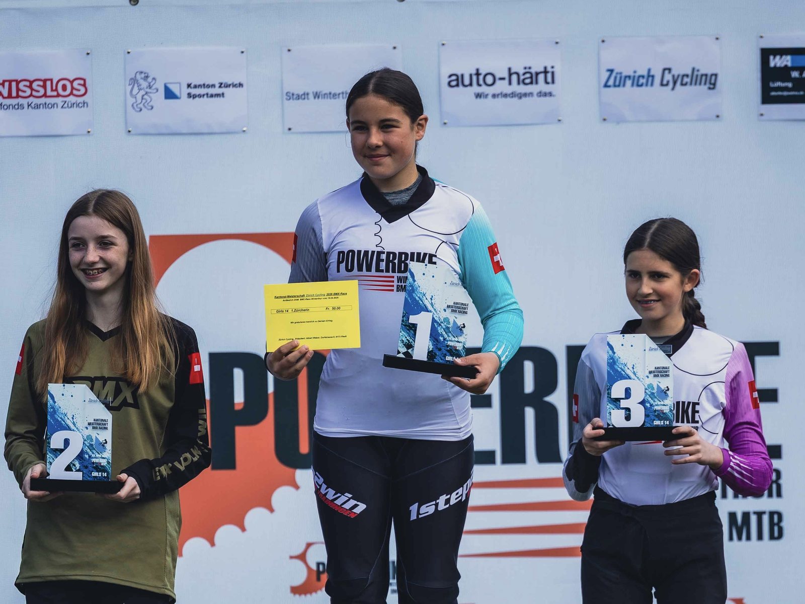Drei Fahrerinnen auf dem Podest der Zürcher Kantonalmeisterschaft — zuoberst eine Powerbike-Fahrerin mit Pokal und Siegerurkunde